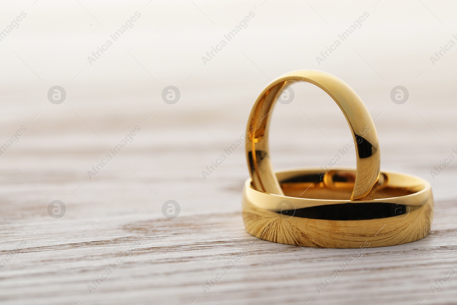 Photo of Beautiful golden wedding rings on wooden table, closeup. Space for text