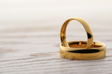 Photo of Beautiful golden wedding rings on wooden table, closeup. Space for text