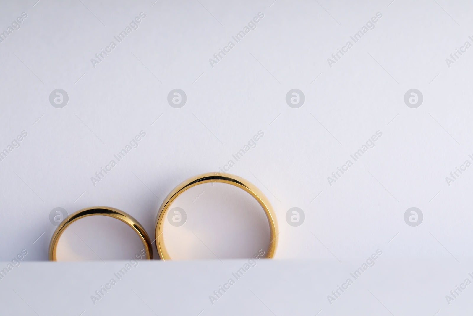 Photo of Beautiful golden wedding rings on white background, top view. Space for text