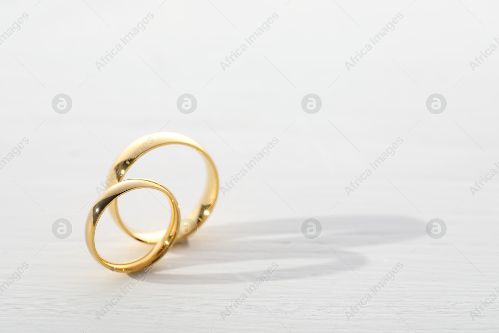 Photo of Beautiful golden wedding rings on light wooden background, space for text