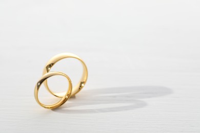 Photo of Beautiful golden wedding rings on light wooden background, space for text