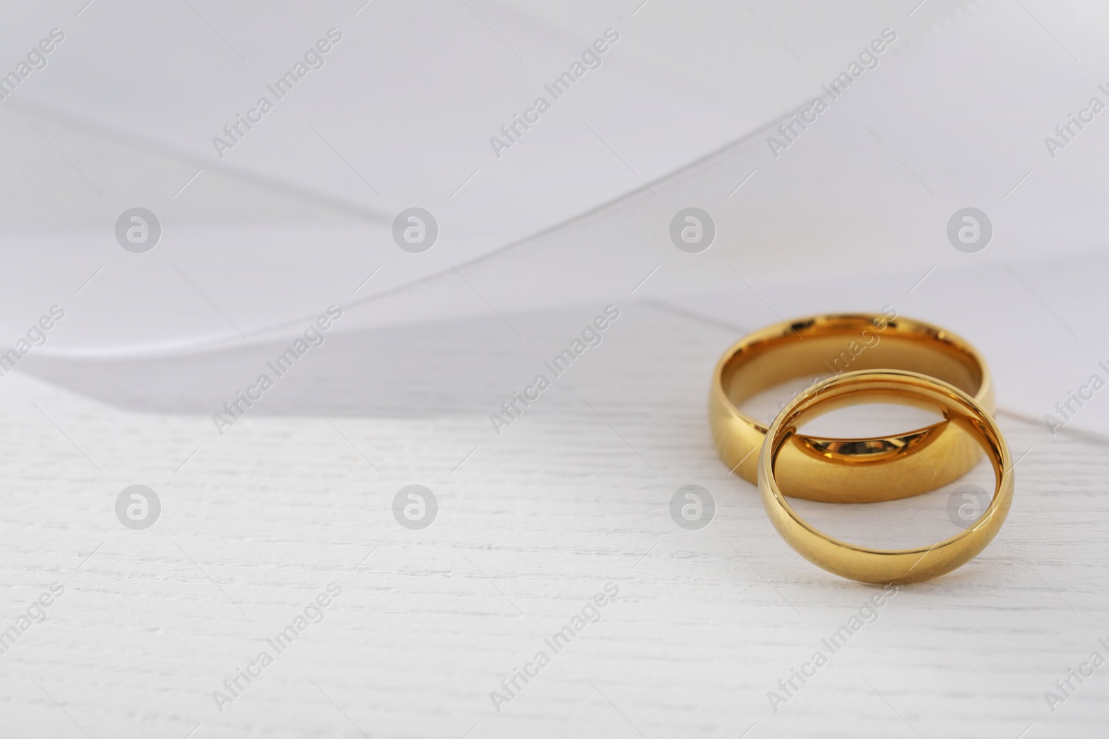 Photo of Beautiful golden wedding rings and white ribbon on light wooden background