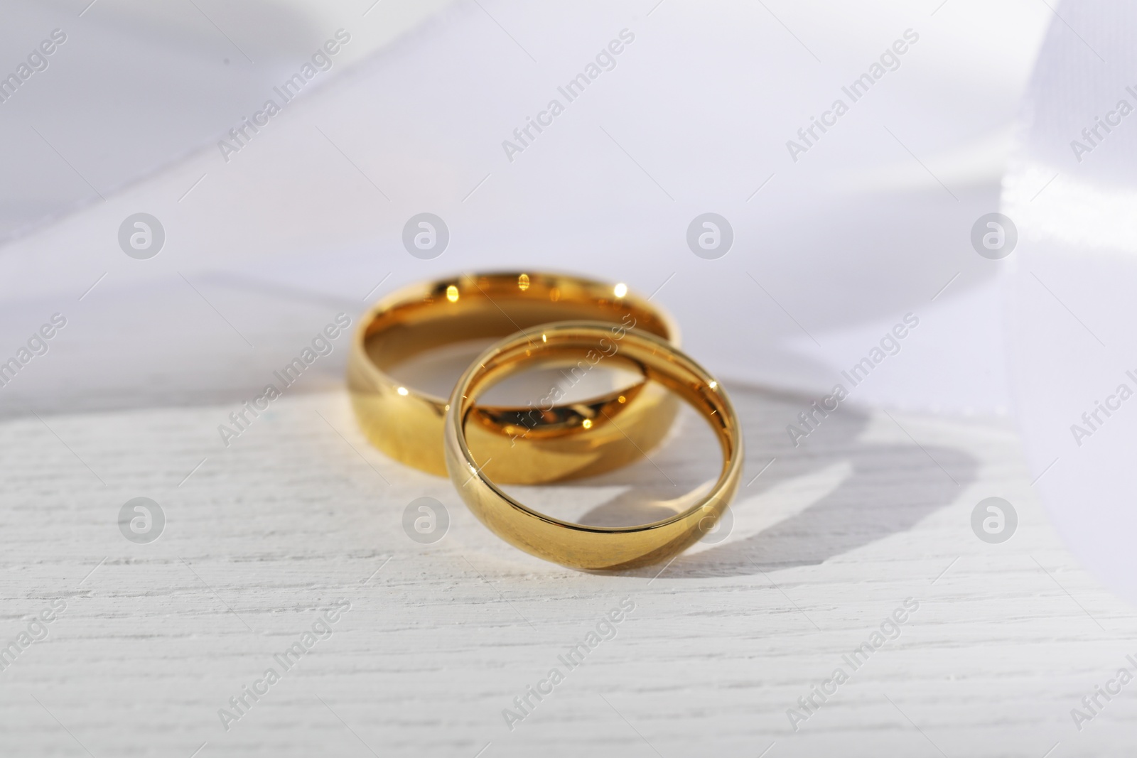 Photo of Beautiful golden wedding rings and white ribbon on light wooden background, closeup