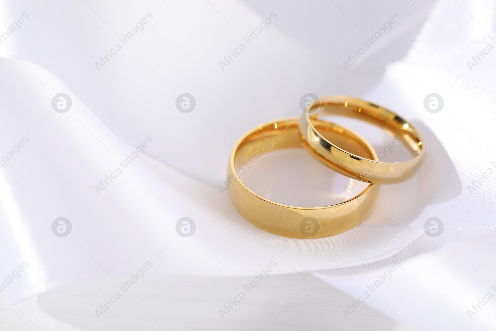 Photo of Beautiful golden wedding rings and white ribbon on light background, closeup