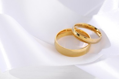 Photo of Beautiful golden wedding rings and white ribbon on light background, closeup