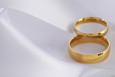 Photo of Beautiful golden wedding rings on white ribbon, closeup