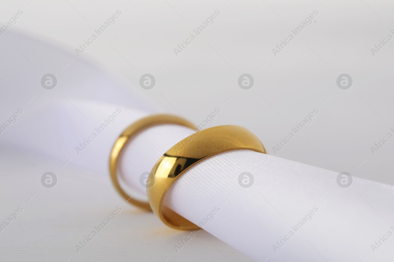 Photo of Beautiful golden wedding rings and white ribbon on light wooden background, closeup