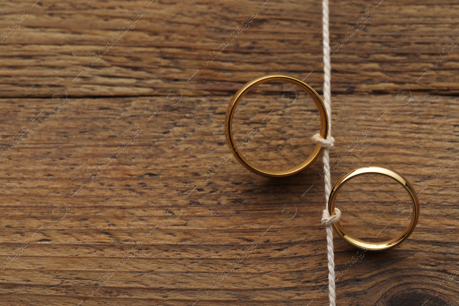 Photo of Beautiful golden wedding rings tied with thread on wooden background, above view. Space for text