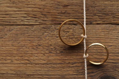 Beautiful golden wedding rings tied with thread on wooden background, above view. Space for text