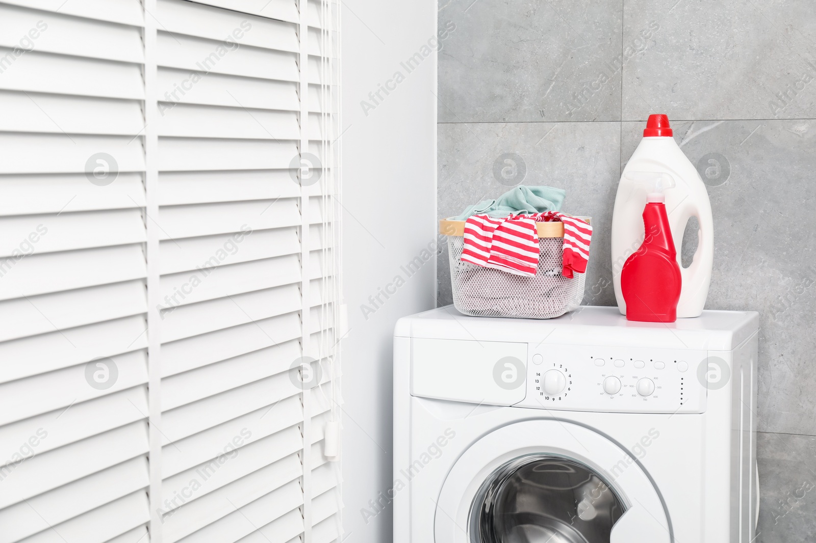 Photo of Different detergents and basket with laundry on washing machine indoors