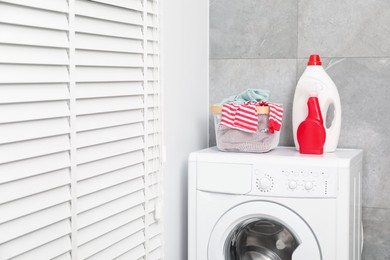 Photo of Different detergents and basket with laundry on washing machine indoors