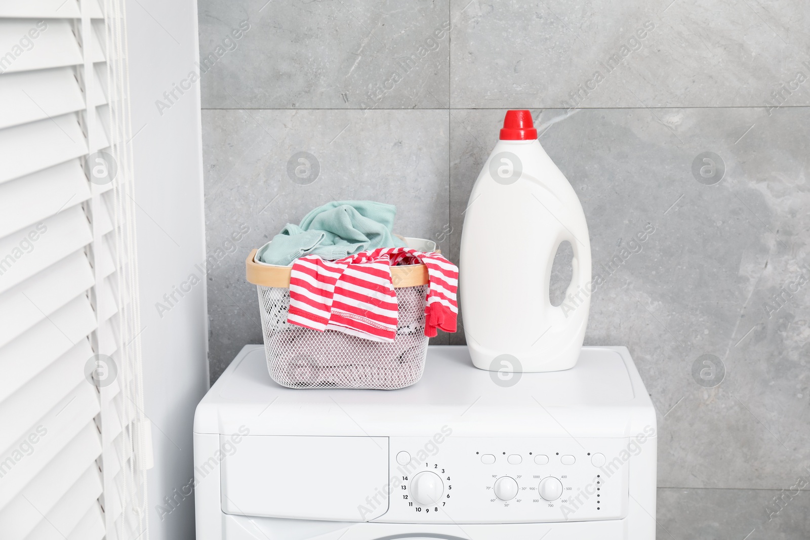 Photo of Detergent and basket with laundry on washing machine indoors