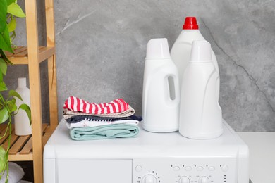 Photo of Laundry detergents in bottles and stacked clean clothes on washing machine indoors