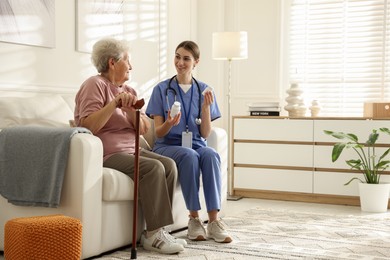 Photo of Caregiver giving pills to senior woman on sofa indoors. Home health care service