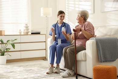 Photo of Caregiver giving pills to senior woman on sofa indoors. Home health care service