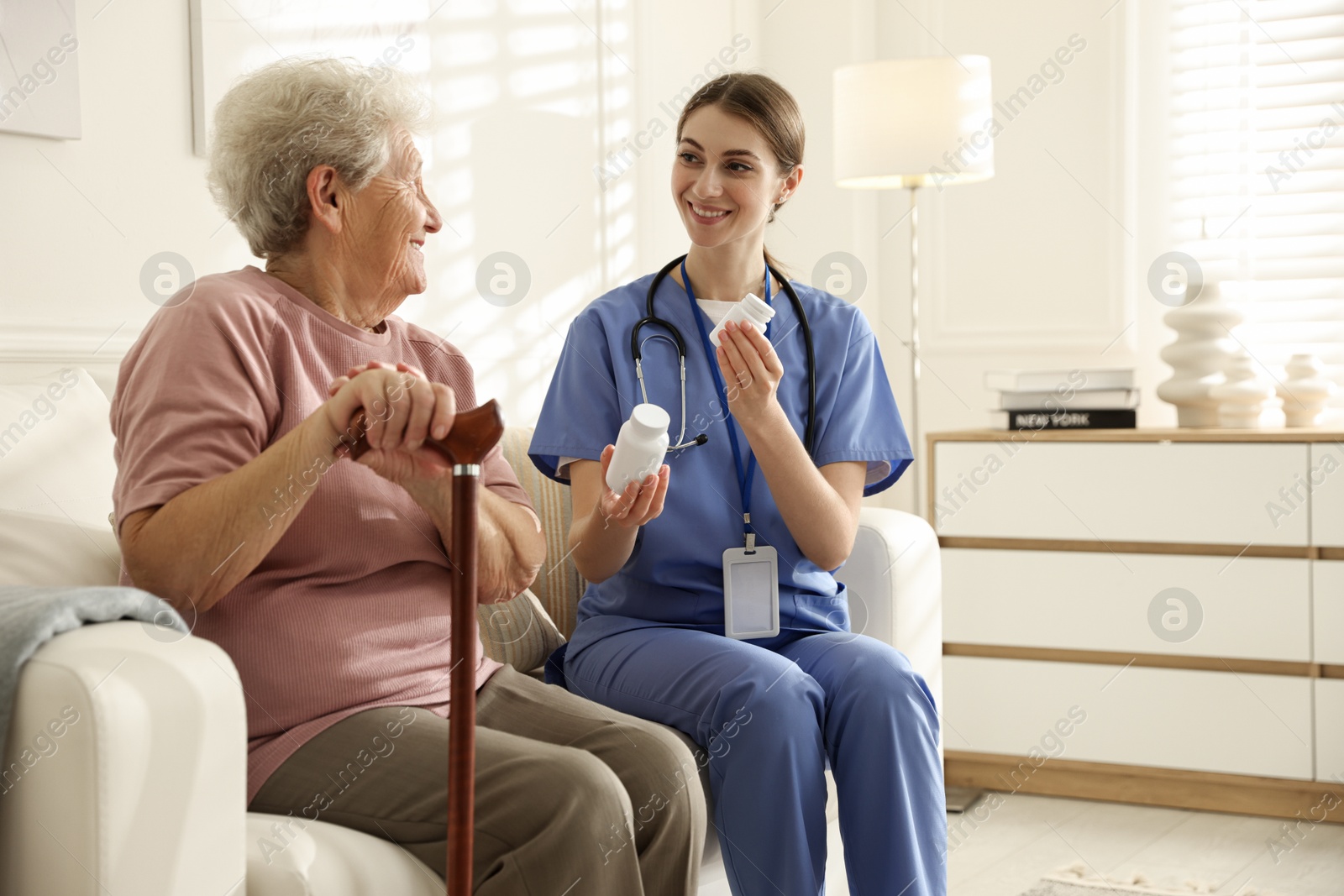 Photo of Caregiver giving pills to senior woman on sofa indoors. Home health care service