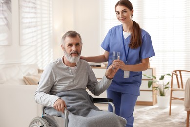 Photo of Caregiver giving glass of water to senior man indoors. Home health care service