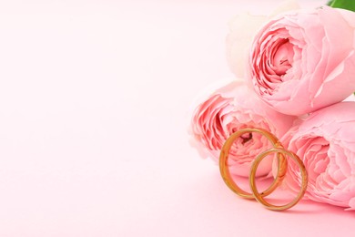 Photo of Golden wedding rings and flowers on pink background, closeup. Space for text