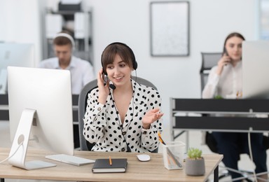 Photo of Saleswoman talking to client via headset at desk in office