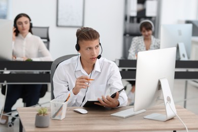 Photo of Salesman making notes while talking to client via headset at desk in office