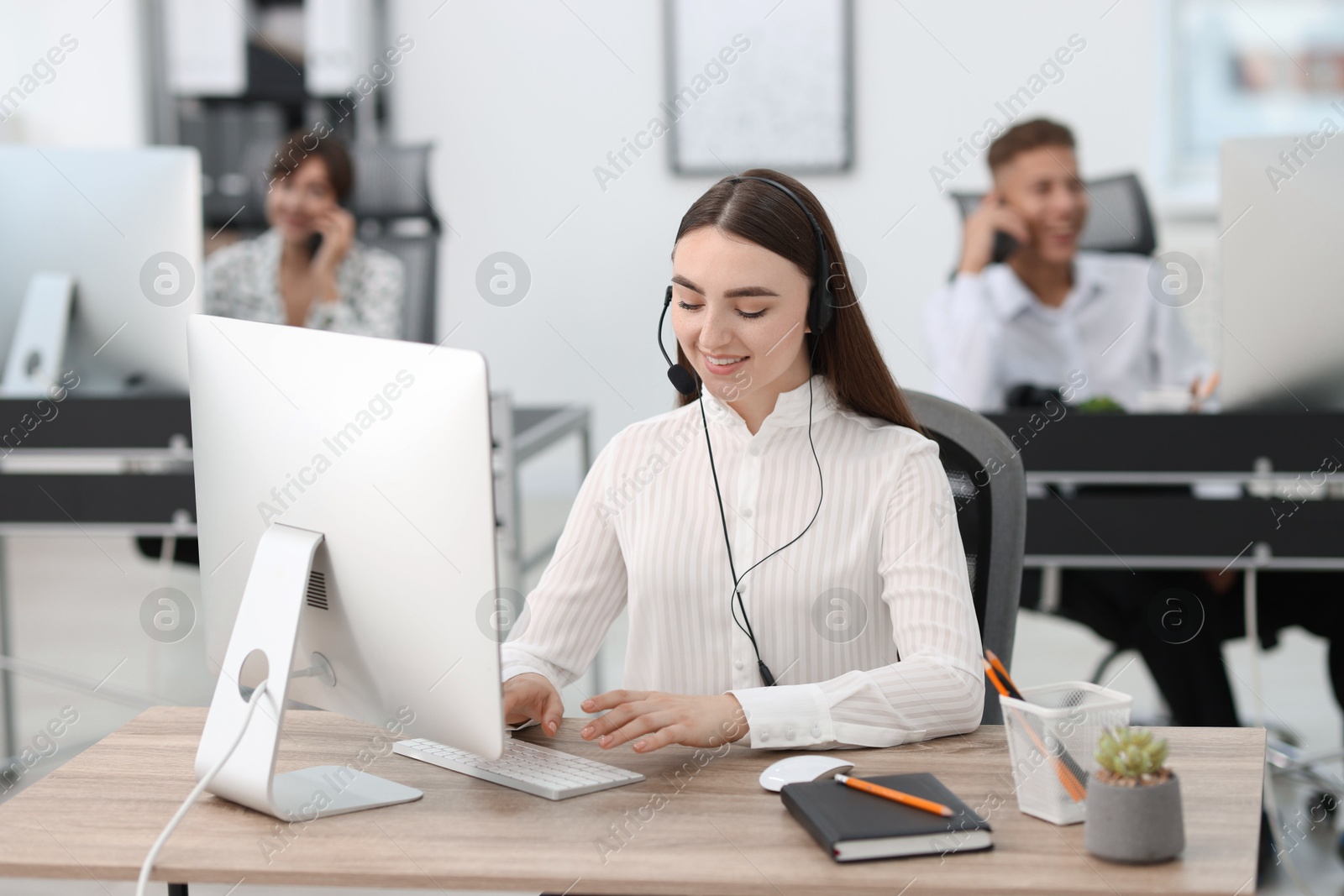 Photo of Saleswoman talking to client via headset at desk in office