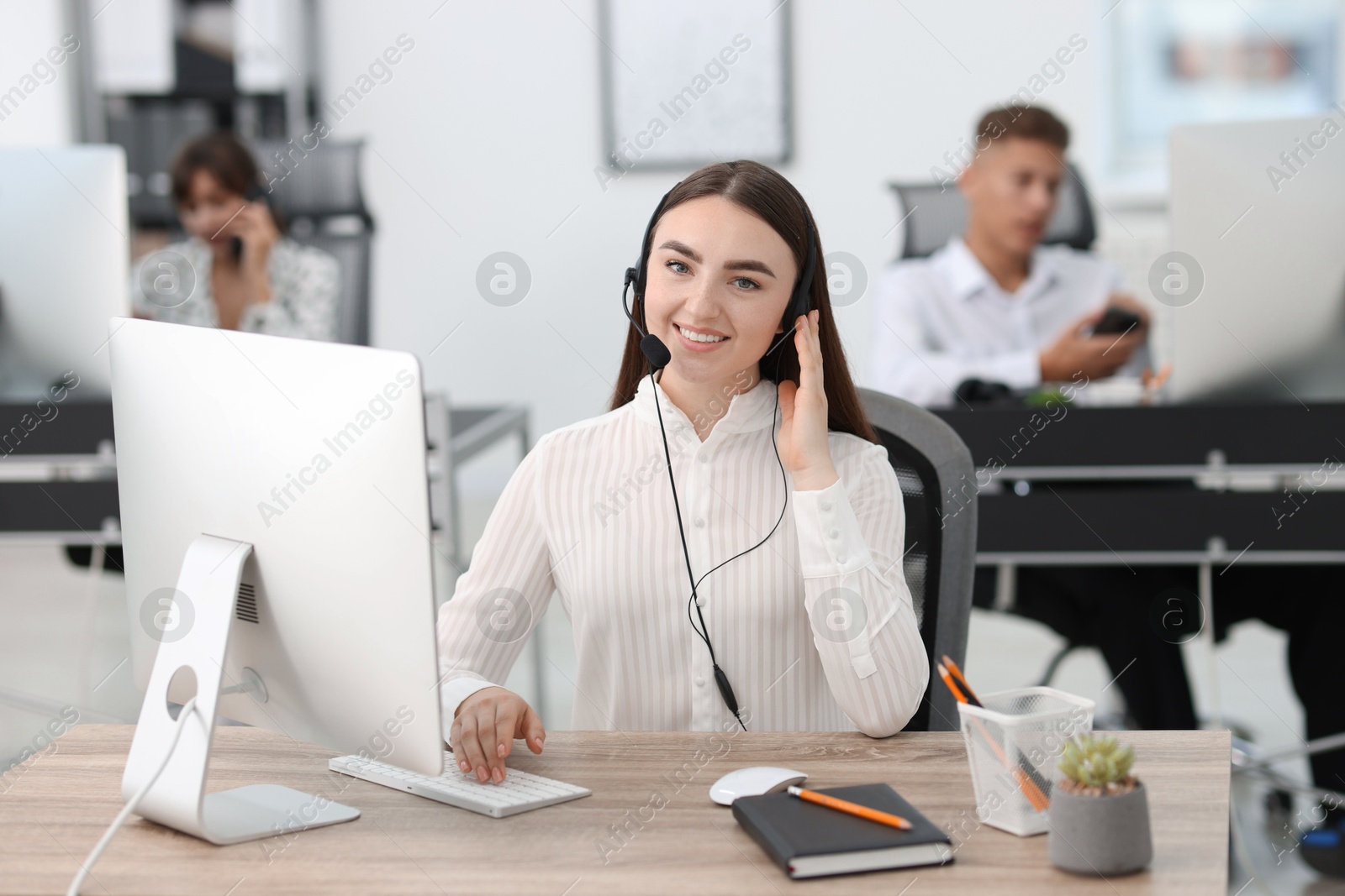 Photo of Saleswoman talking to client via headset at desk in office