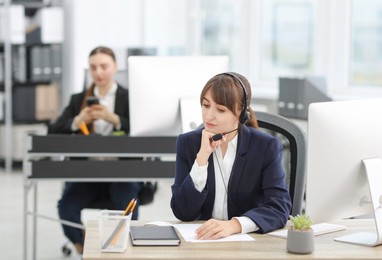 Photo of Saleswoman talking to client via headset at desk in office