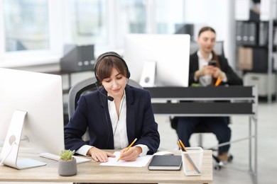 Photo of Saleswoman talking to client via headset at desk in office