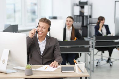 Photo of Salesman talking to client via headset at desk in office