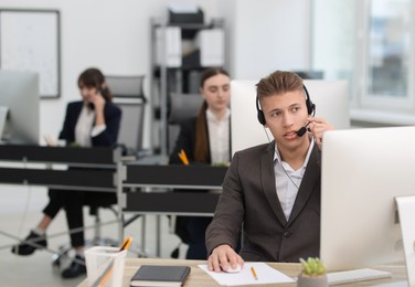 Photo of Salesman talking to client via headset at desk in office