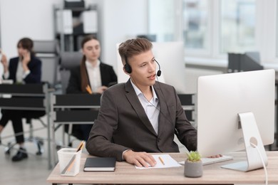 Photo of Salesman talking to client via headset at desk in office