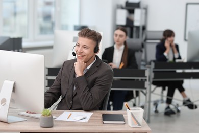 Photo of Salesman talking to client via headset at desk in office