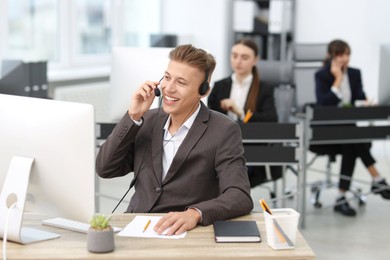 Photo of Salesman talking to client via headset at desk in office