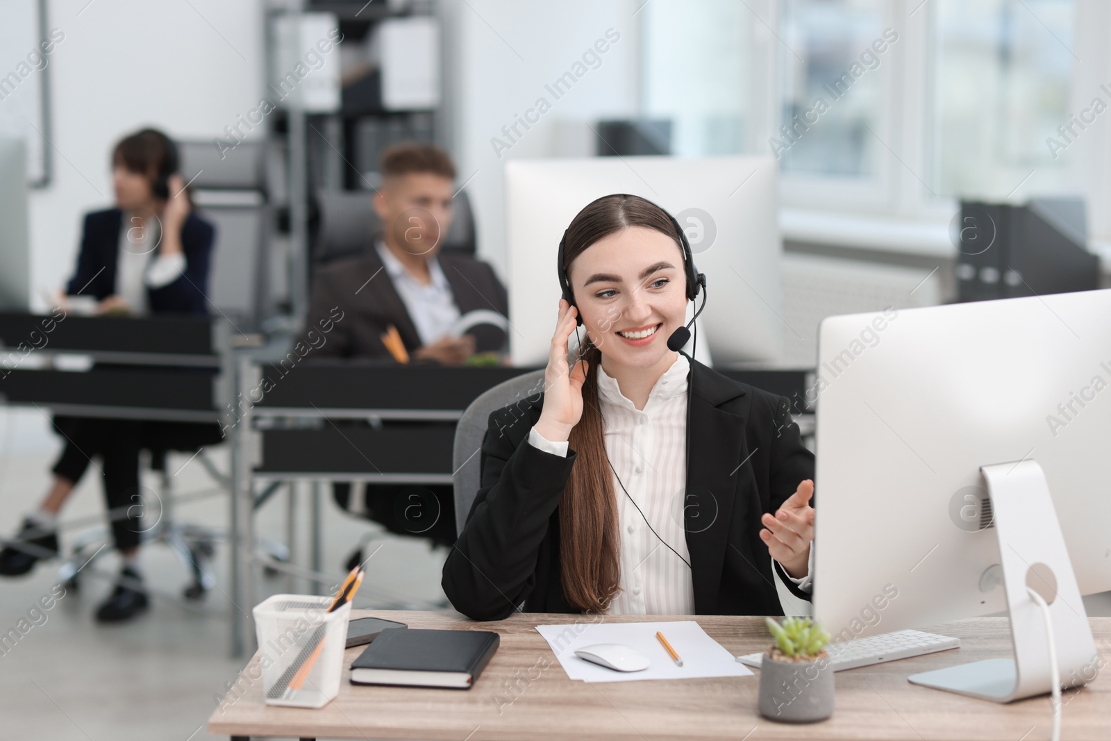 Photo of Saleswoman talking to client via headset at desk in office