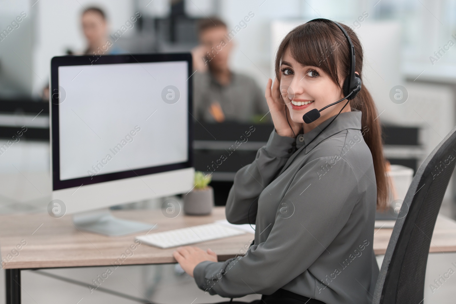 Photo of Saleswoman talking to client via headset at desk in office