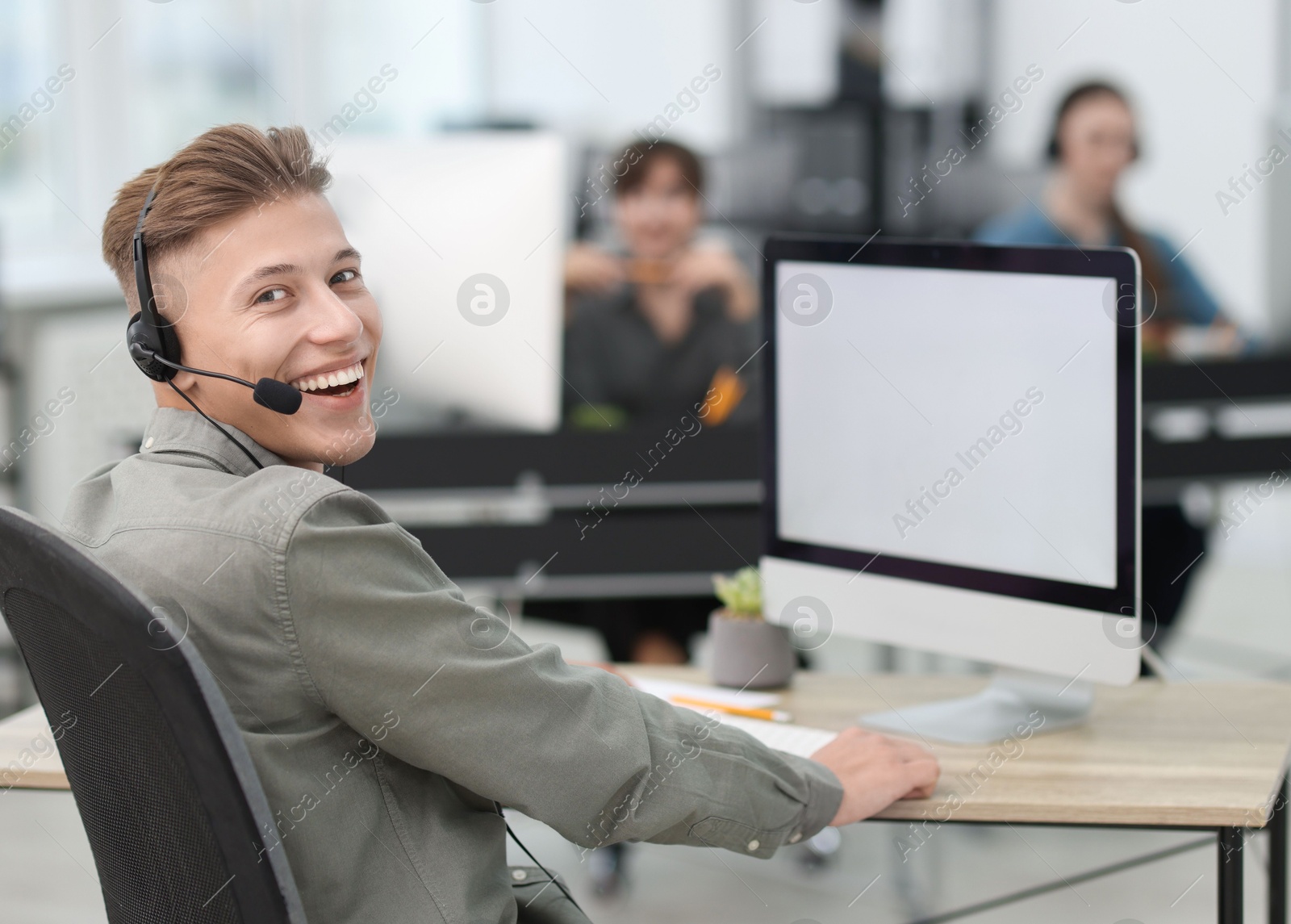 Photo of Salesman talking to client via headset at desk in office