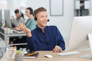 Photo of Salesman talking to client via headset at desk in office