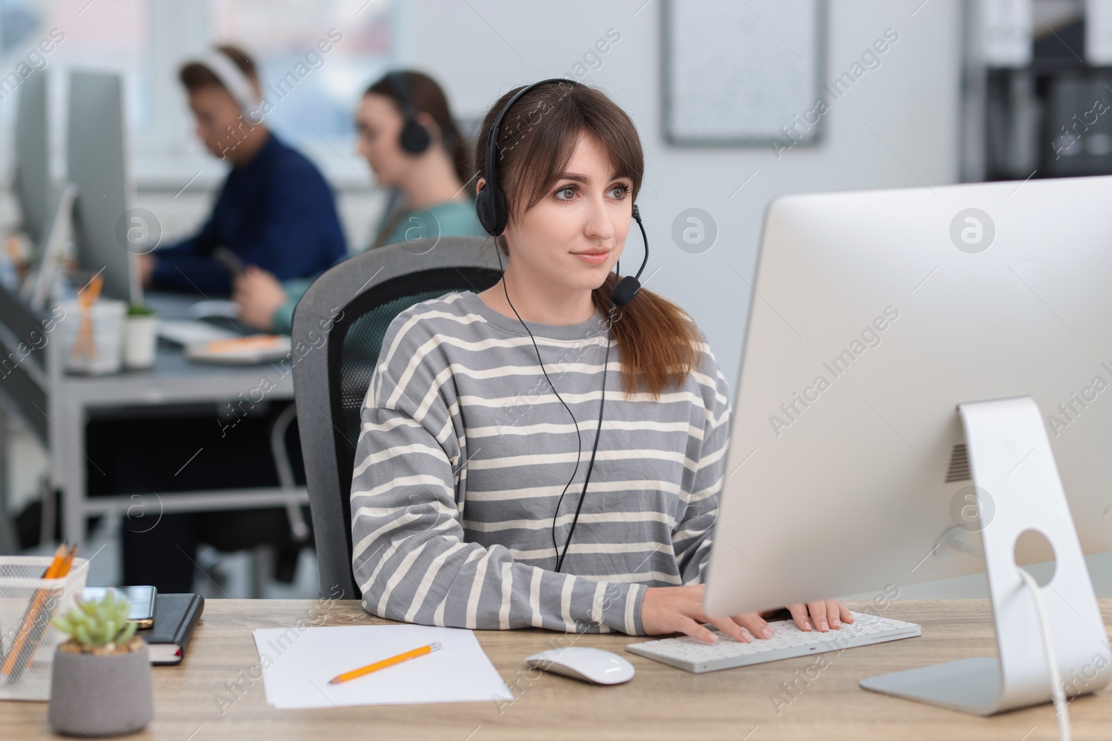 Photo of Saleswoman talking to client via headset at desk in office