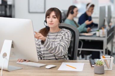 Photo of Saleswoman talking to client via headset at desk in office