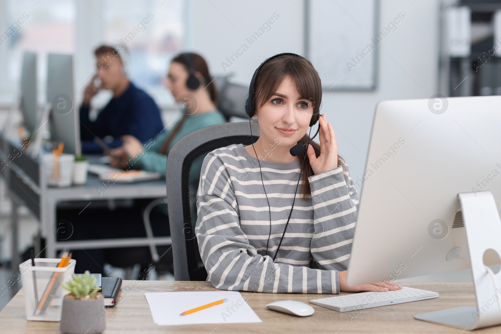 Photo of Saleswoman talking to client via headset at desk in office