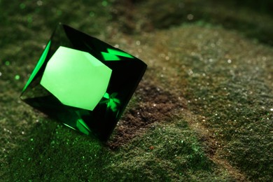 Photo of Beautiful shiny green gemstone on stone, closeup. Space for text