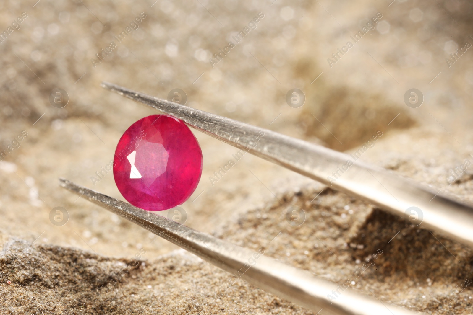 Photo of Tweezers with beautiful pink gemstone on stone, closeup