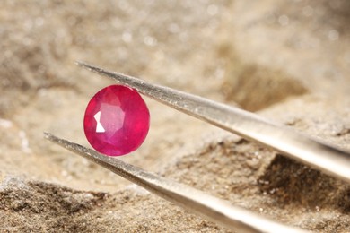 Photo of Tweezers with beautiful pink gemstone on stone, closeup