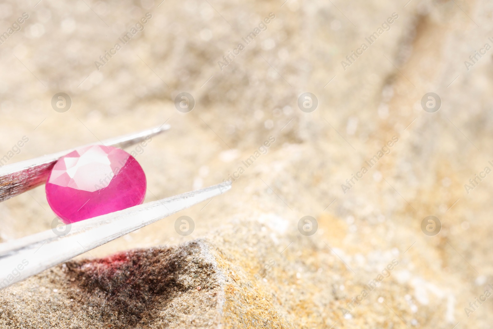 Photo of Tweezers with beautiful pink gemstone on stone, closeup. Space for text