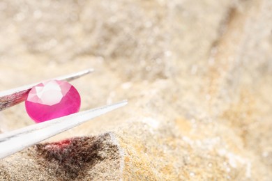 Tweezers with beautiful pink gemstone on stone, closeup. Space for text