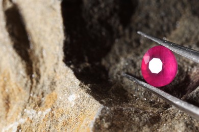 Photo of Tweezers with beautiful pink gemstone on stone, closeup. Space for text