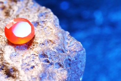 Photo of Beautiful shiny orange gemstone on stone against blue background, space for text