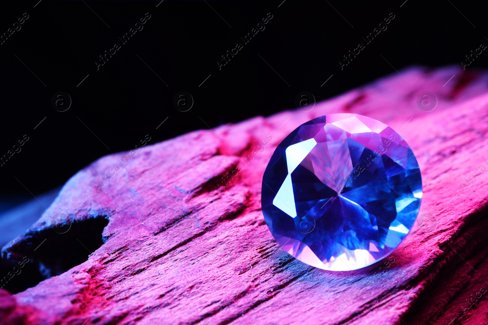 Photo of Beautiful shiny gemstone on stone against dark background, closeup