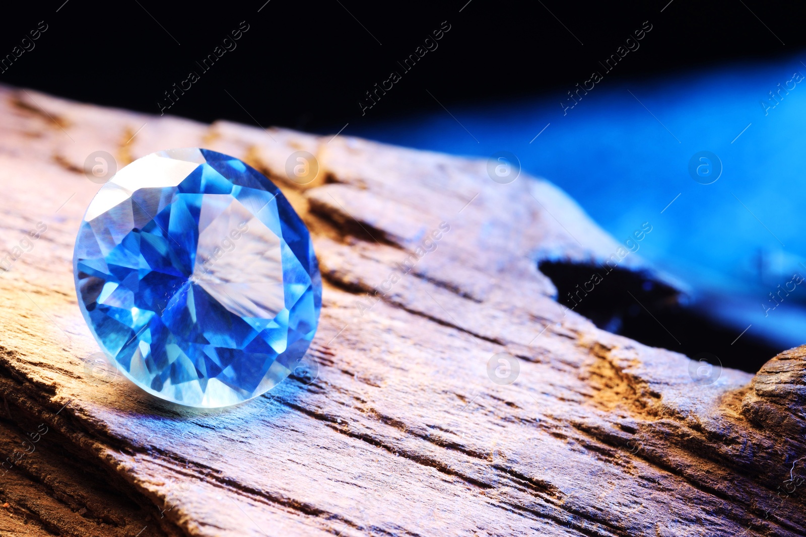 Photo of Beautiful shiny light blue gemstone on stone against dark background, closeup