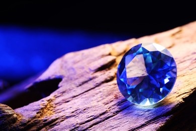 Photo of Beautiful shiny light blue gemstone on stone against dark background, closeup